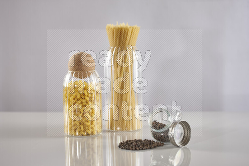 Raw pasta in glass jars with black peppers on light grey background