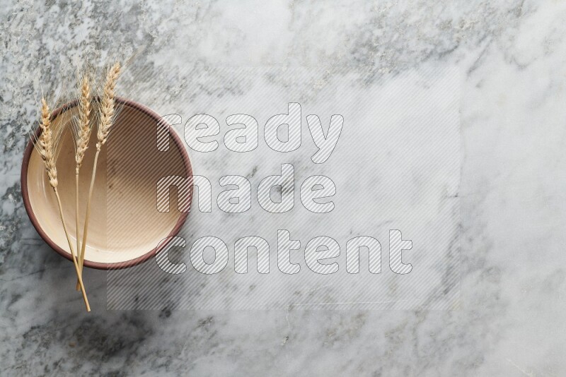 Wheat stalks on beige pottery oven bowl on grey marble background