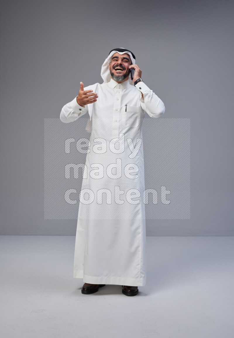 Saudi man Wearing Thob and white Shomag standing talking on phone on Gray background