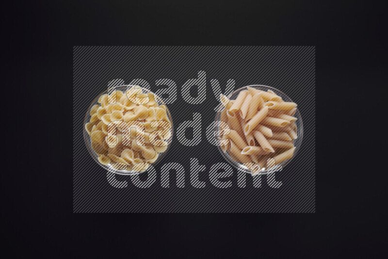Different pasta types in glass bowls on black background