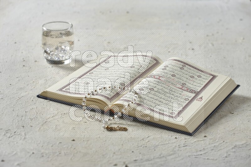 Quran with dates, prayer beads and different drinks all placed on textured white background