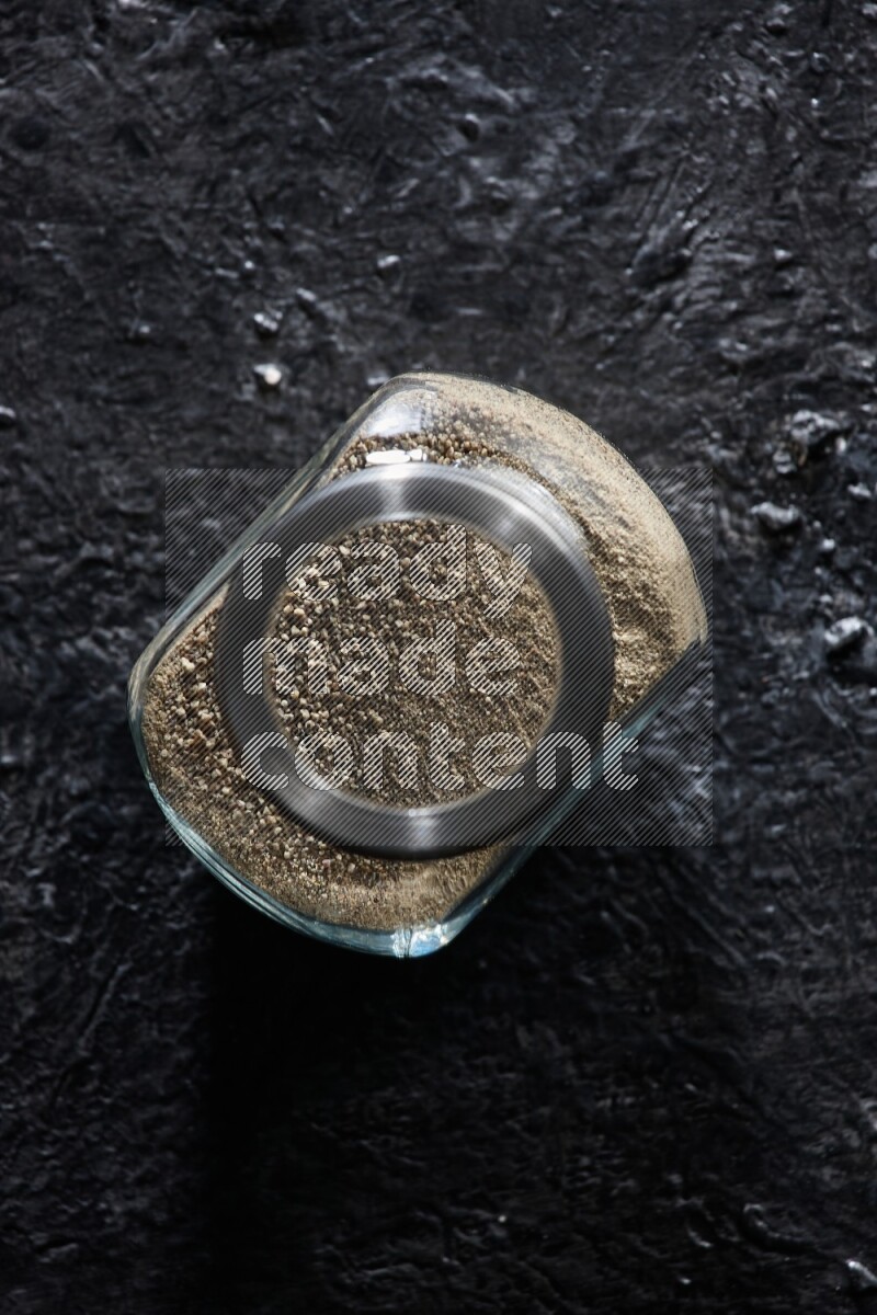 Herbal glass jar full of white pepper on textured black flooring