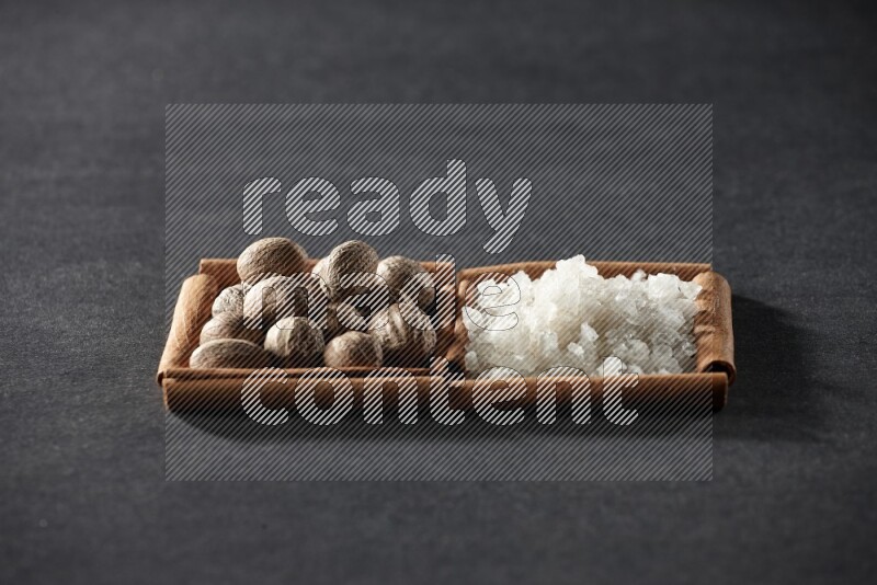 2 squares of cinnamon sticks full of nutmeg and white salt on black flooring