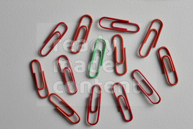 A bunch of red paper clips with a different colored paper clip in the center on grey background