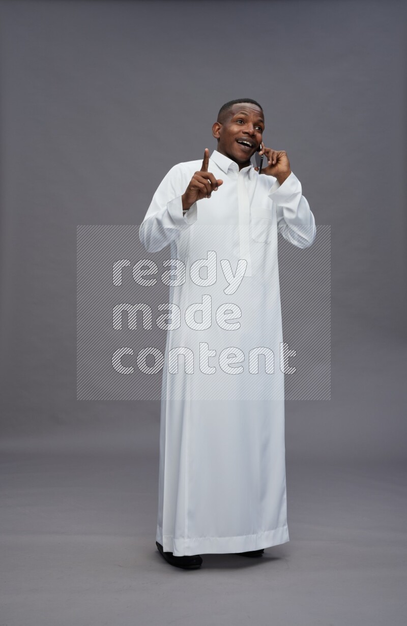 Saudi man wearing thob standing talking on phone on gray background