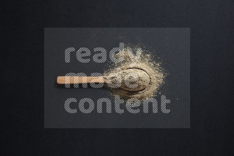 A wooden spoon full of cardamom powder and powder spreaded on black flooring