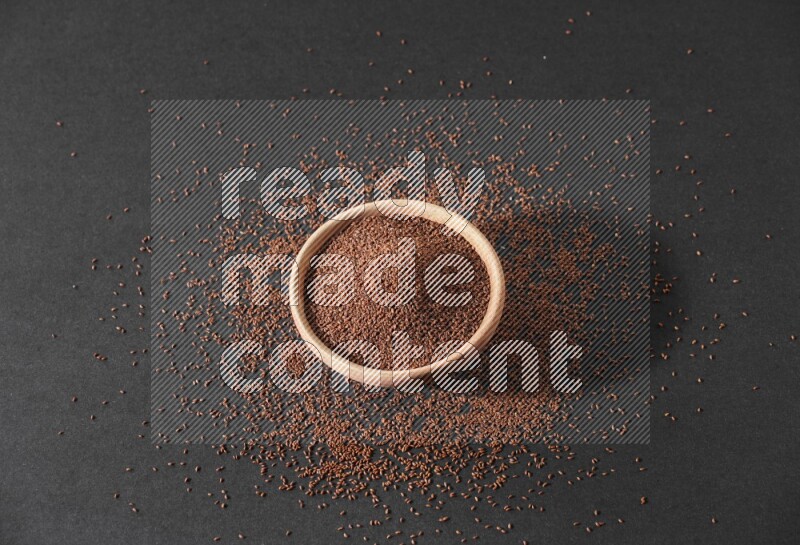 وعاء خشبي ممتلئ ببذور حب الرشاد محاط ببعض البذور علي خلفية سوداء