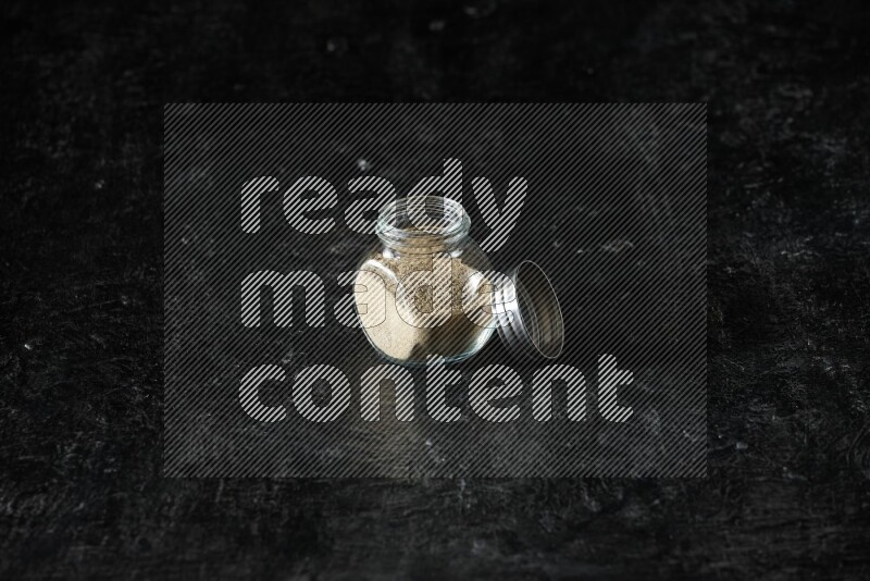 وعاء زجاجي للتوابل ممتلئ ببودرة الهيل على خلفية سوداء