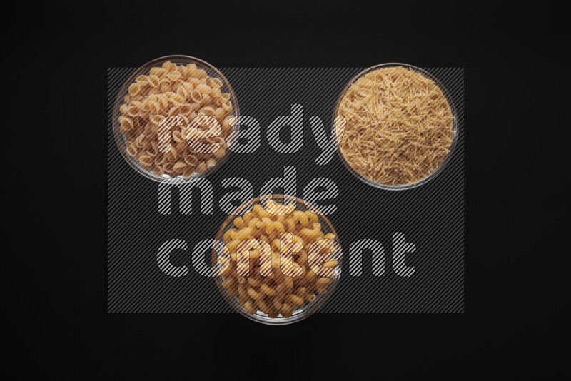 Different pasta types in glass bowls on black background