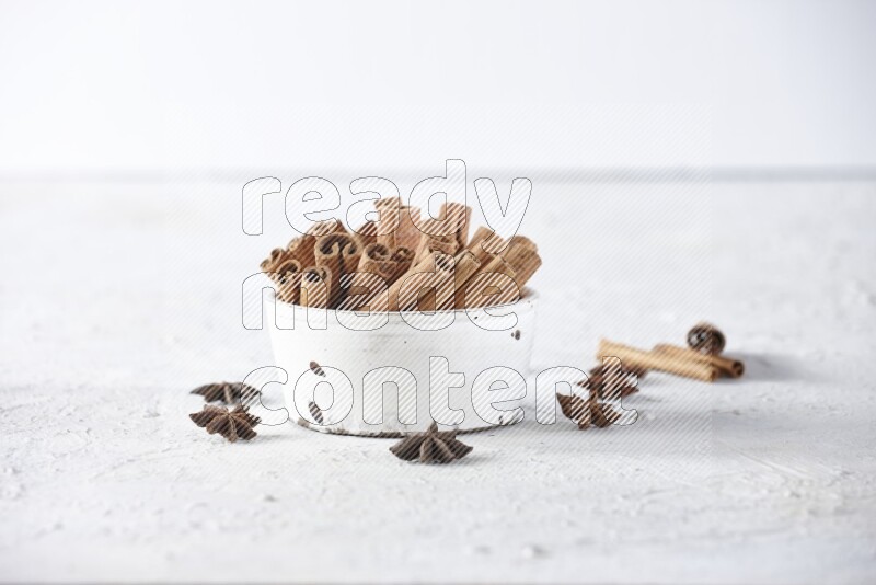 White bowl full of cinnamon sticks surrounded by star anis on a textured white background in different angles