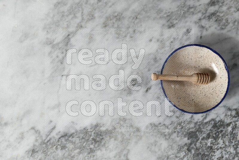 Multicolored pottery bowl with wooden honey dipper in it on grey marble background