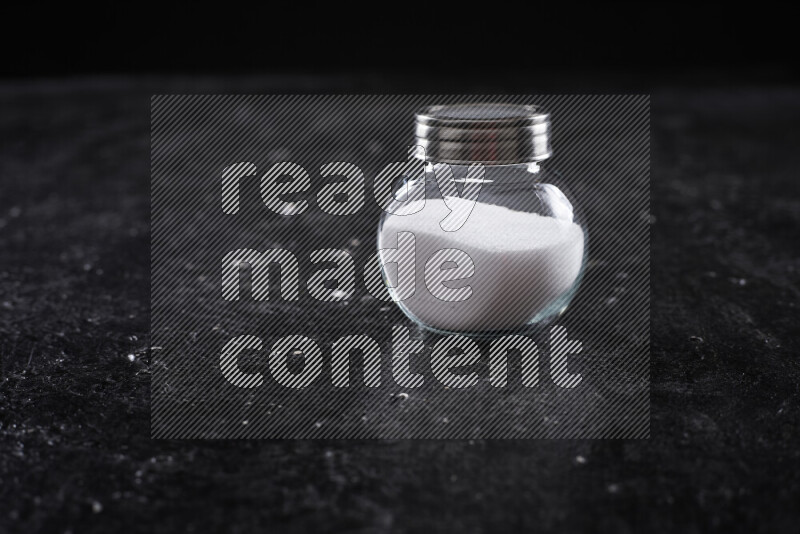 A glass jar full of fine table salt on black background