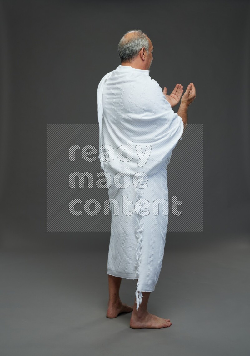 A man wearing Ehram Standing dua'a on gray background