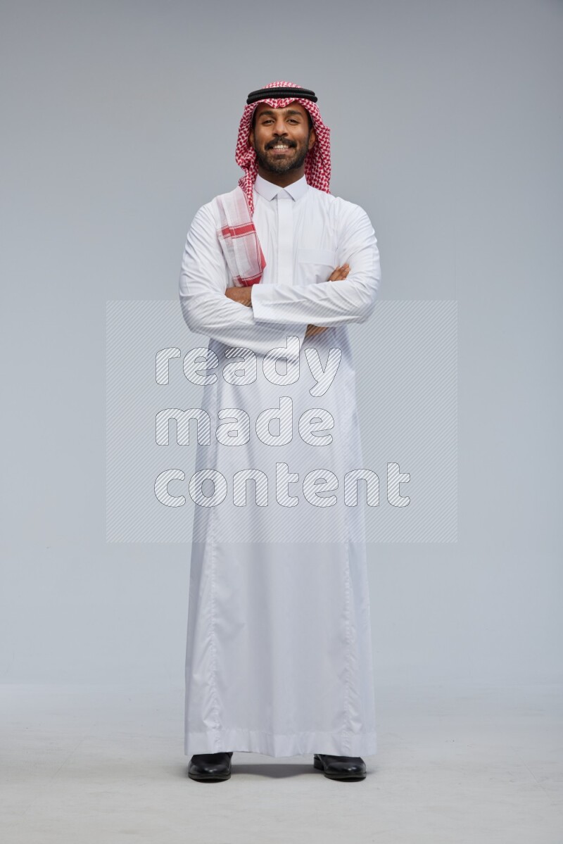 Saudi man Wearing Thob and shomag standing with crossed arms on Gray background