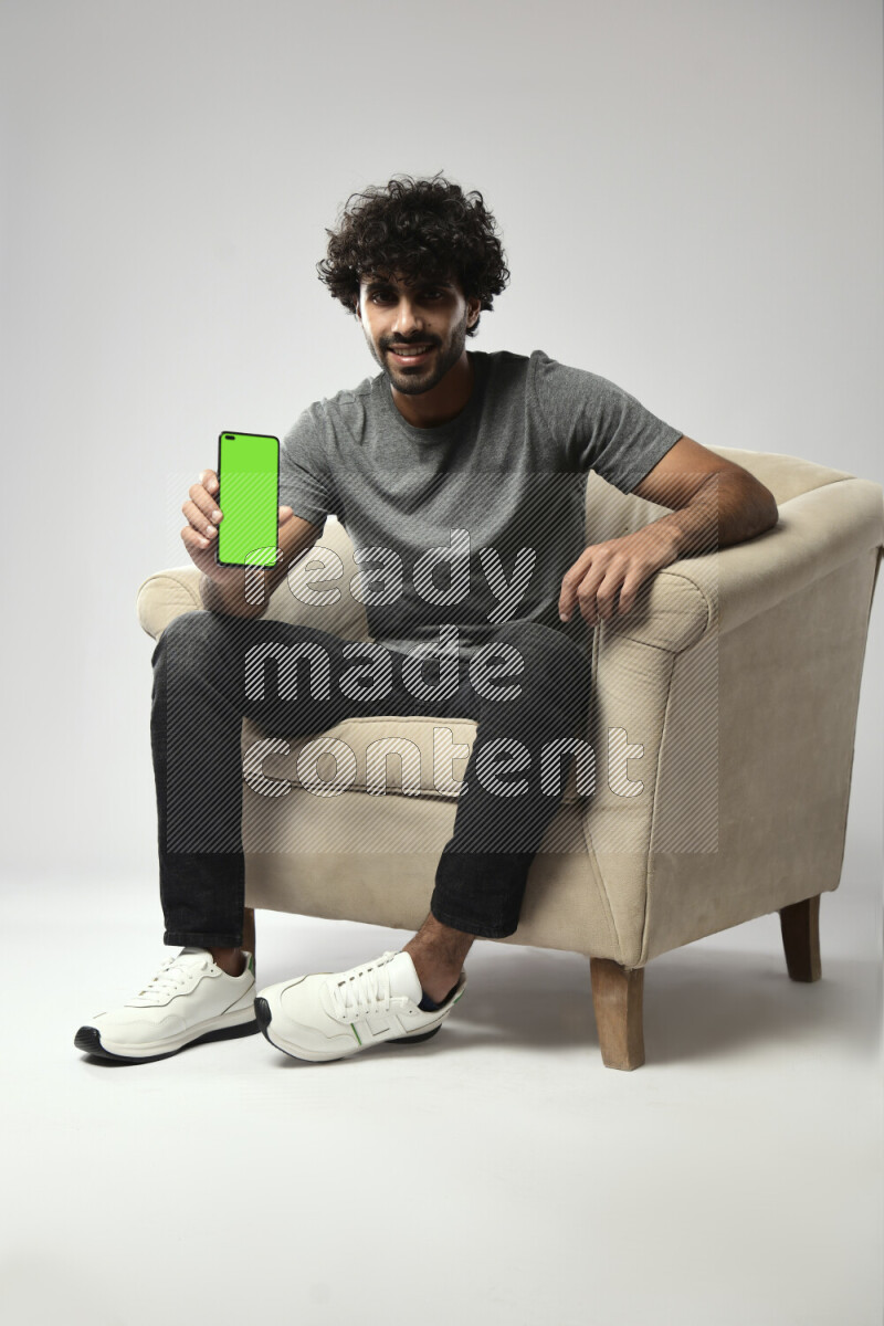 A man wearing casual sitting on a chair showing a phone screen on white background