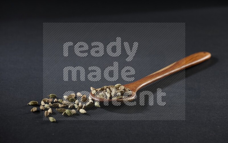 A wooden ladle full of cardamom on black flooring