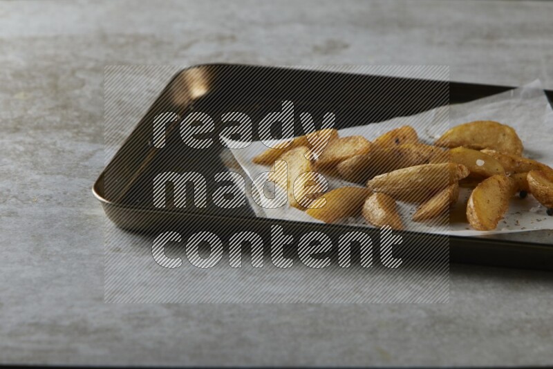 wedges potato on parchment paper in a black stainless steel rectangle tray on grey textured counter top