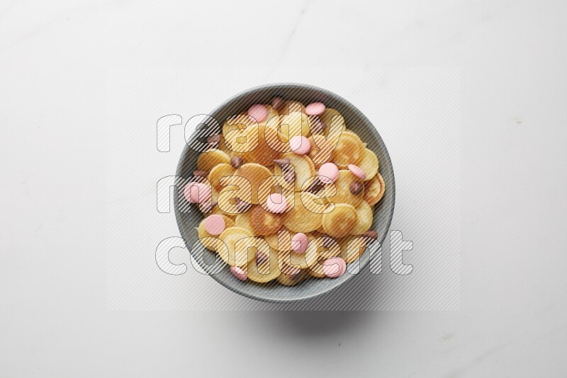 Top-view shot of mixed chocolate chips cereal pancakes in a round bowl on white background