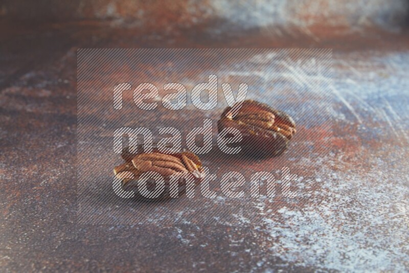 two pecan stuffed madjoul dates on a rustic reddish background