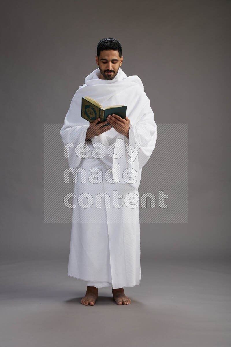 A man wearing Ehram Standing reading quran on gray background