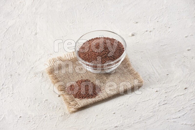 A glass bowl full of garden cress seeds on a burlap fabric on textured white flooring