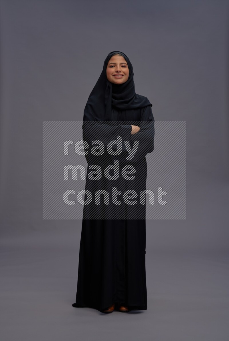 Saudi woman wearing Abaya standing with crossed arms on gray background