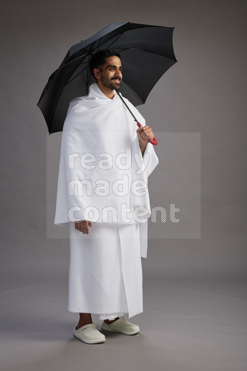 A man wearing Ehram Standing holding umbrella on gray background