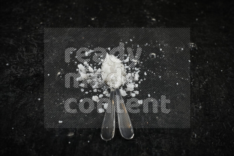 2 metal spoons filled with white salt on black background