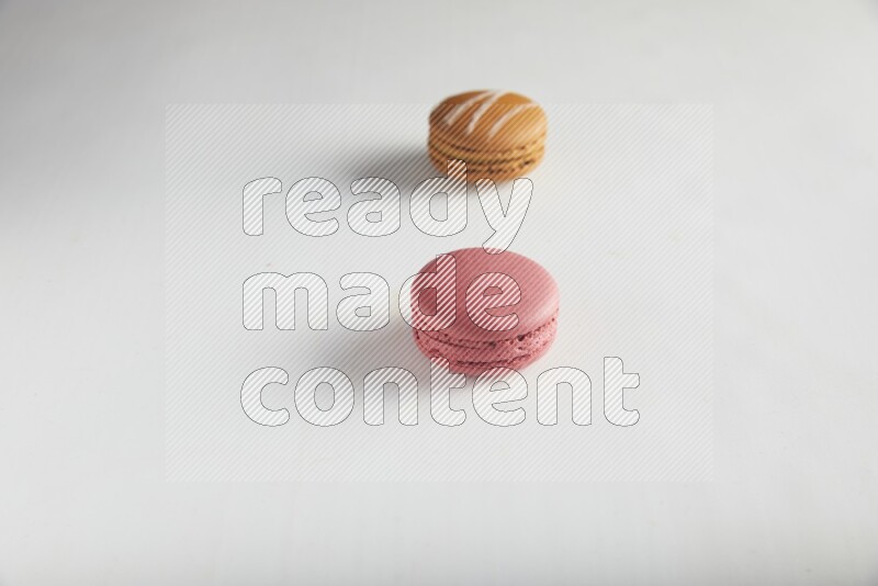 45º Shot of of two assorted Brown Irish Cream, and Pink Raspberry macarons on white background