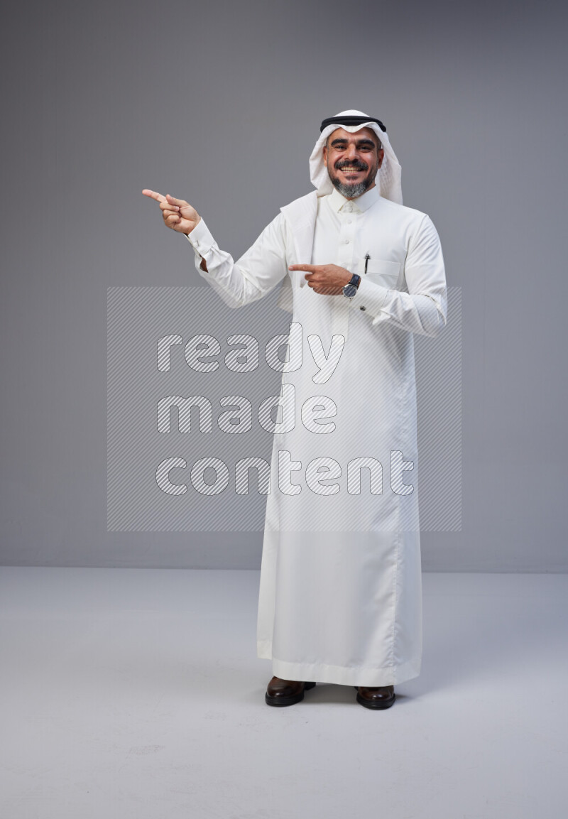 Saudi man Wearing Thob and white Shomag standing interacting with the camera on Gray background