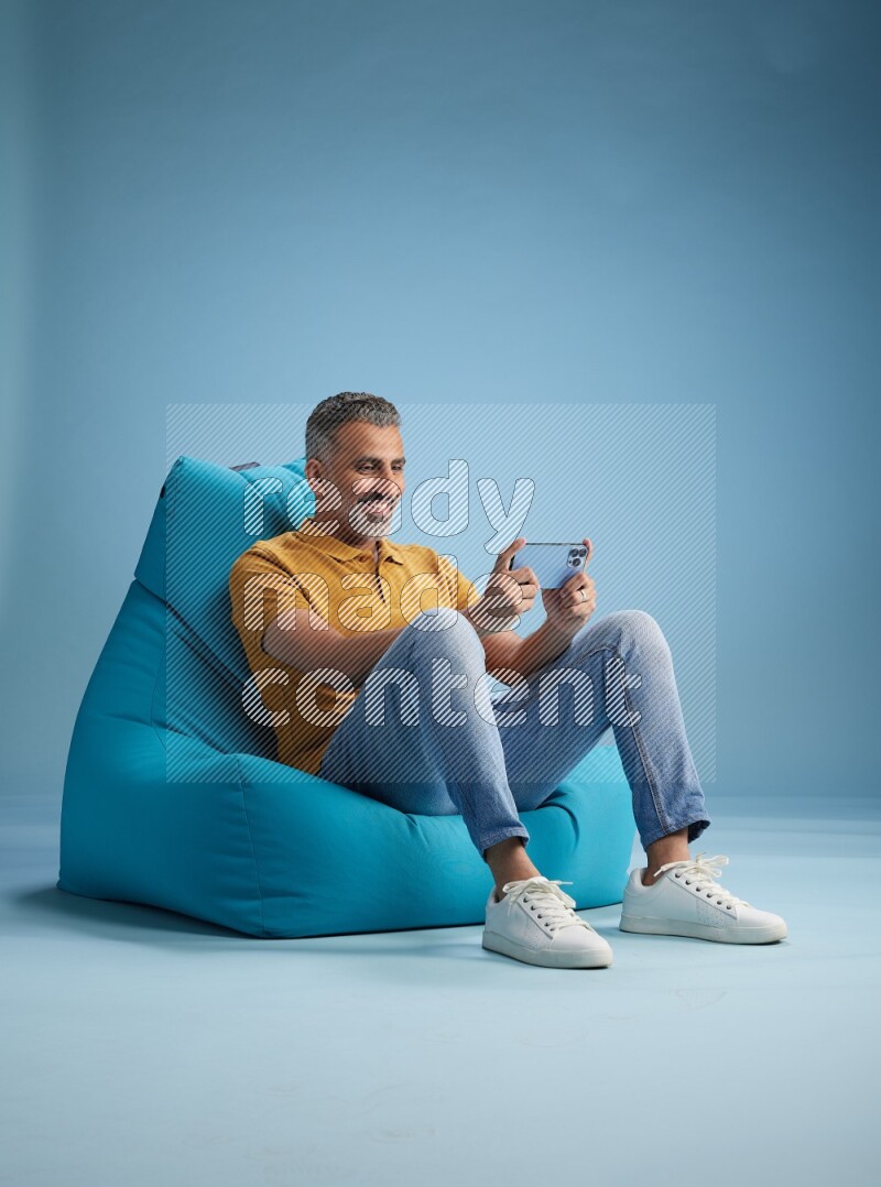 A man sitting on a blue beanbag and playing on phone