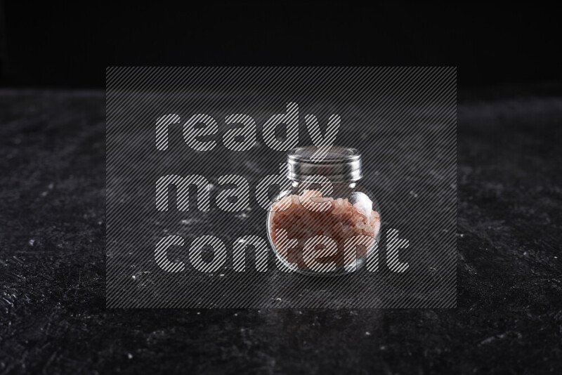 A glass jar full of coarse himalayan salt crystals on black background