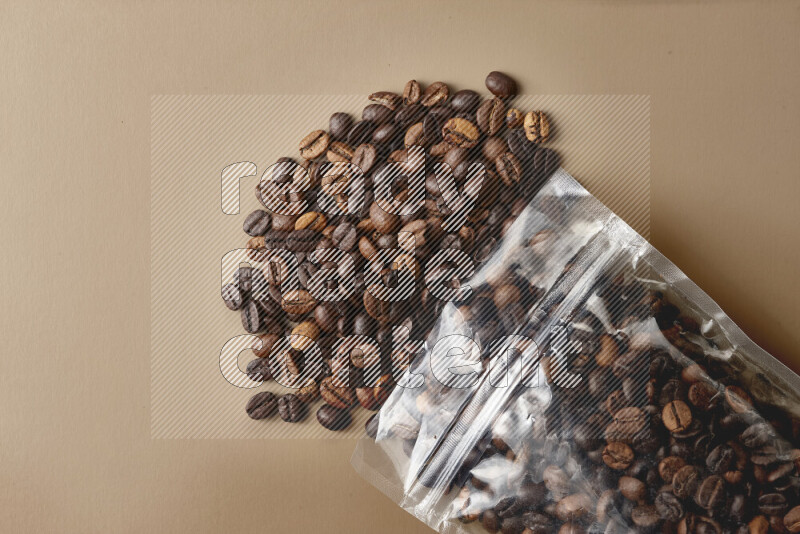 Spilled roasted coffee beans from its pack on beige background