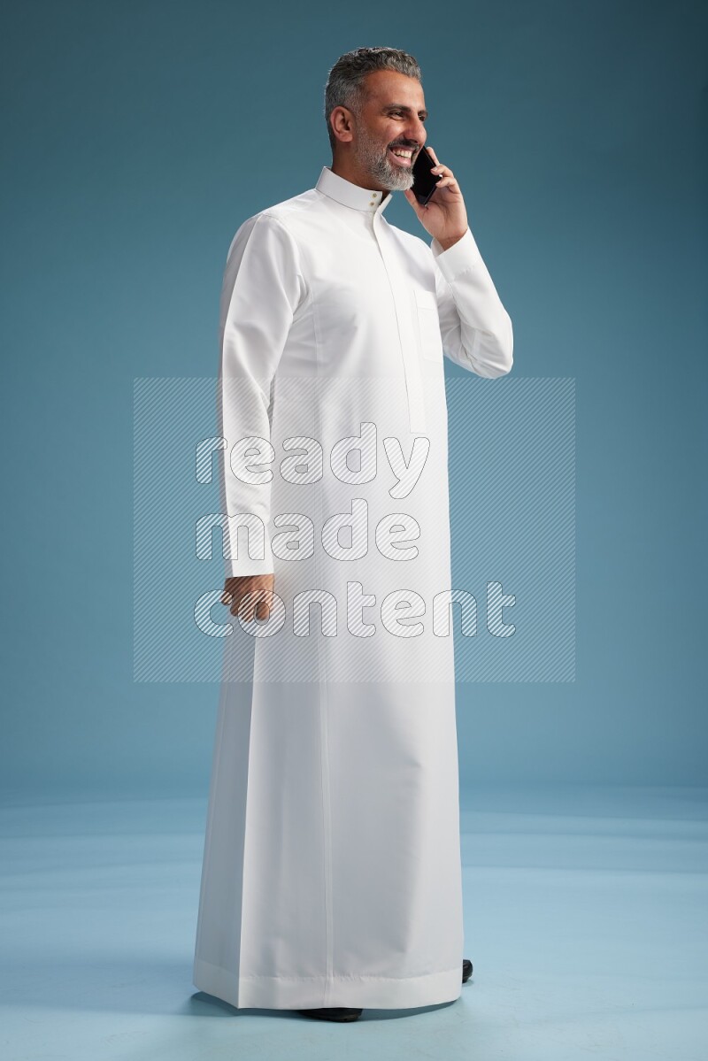 Saudi man wearing thob talking on the phone on blue background