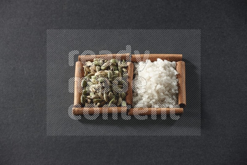 مربعان من أعواد القرفة ممتلئان بالملح الأبيض وحبوب الهيل علي خلفية سوداء