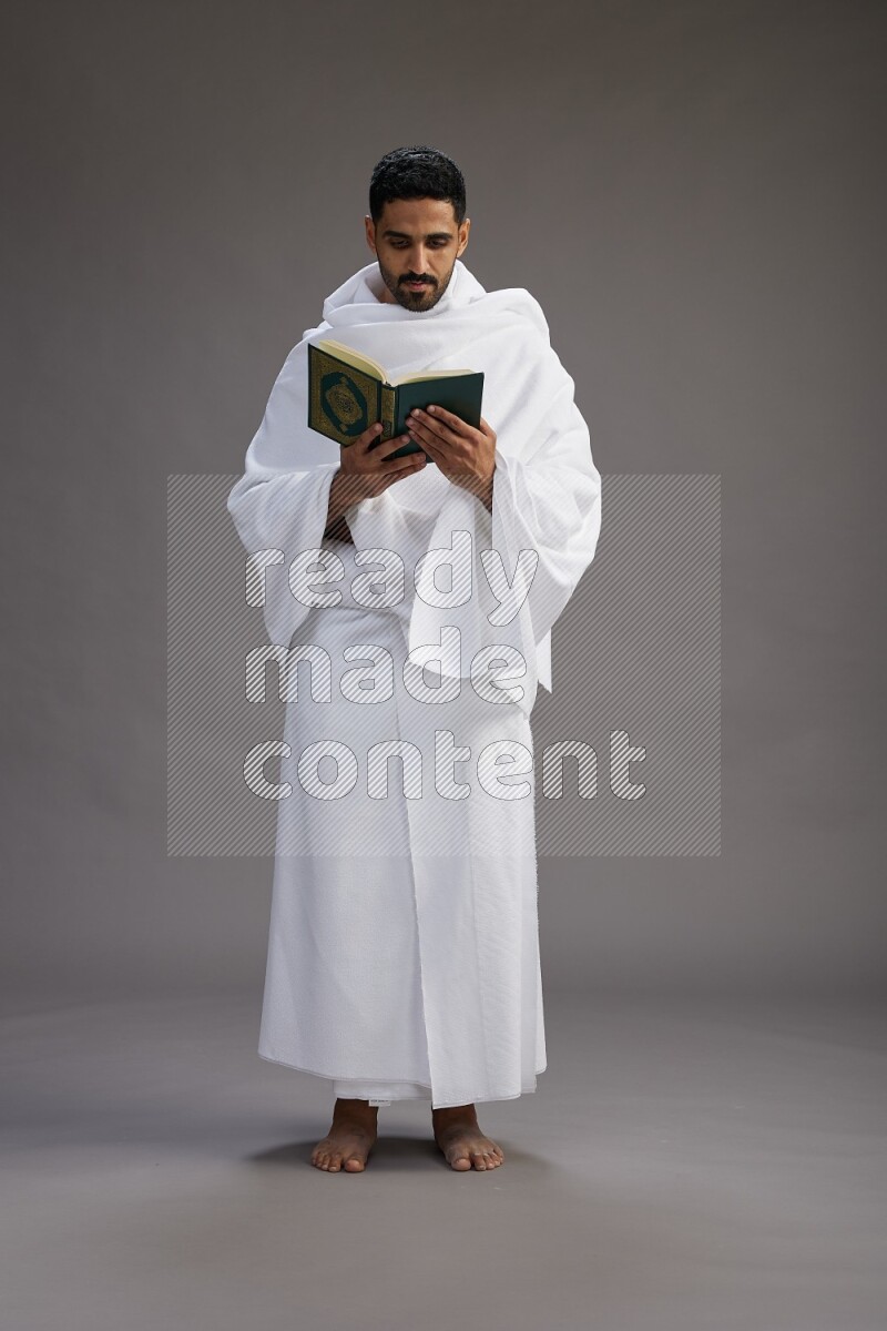 A man wearing Ehram Standing reading quran on gray background