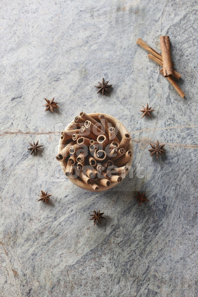 wooden bowl full of cinnamon sticks surrounded by star anis on marble background in different angles
