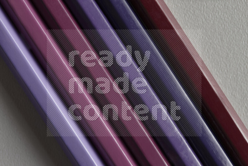 A collection of colored pencils arranged showcasing a gradient of purple hues on grey background