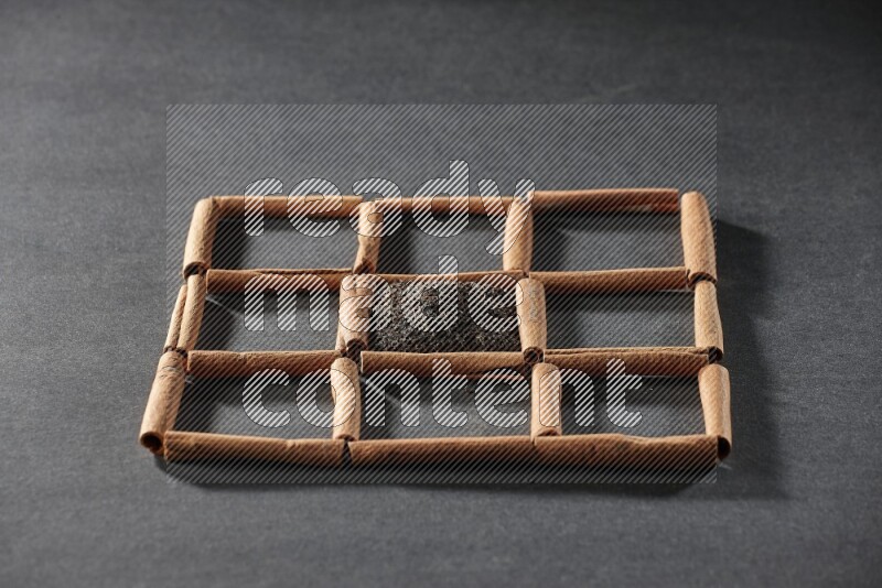 9 squares of cinnamon sticks full of tea in the middle surrounded by nutmeg, dried mint, cloves, dried basil, dried ginger, cinnamon, star anise and cardamom on black flooring