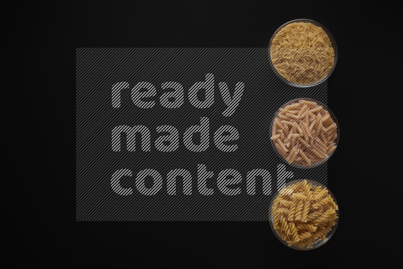 Different pasta types in 3 glass bowls on black background