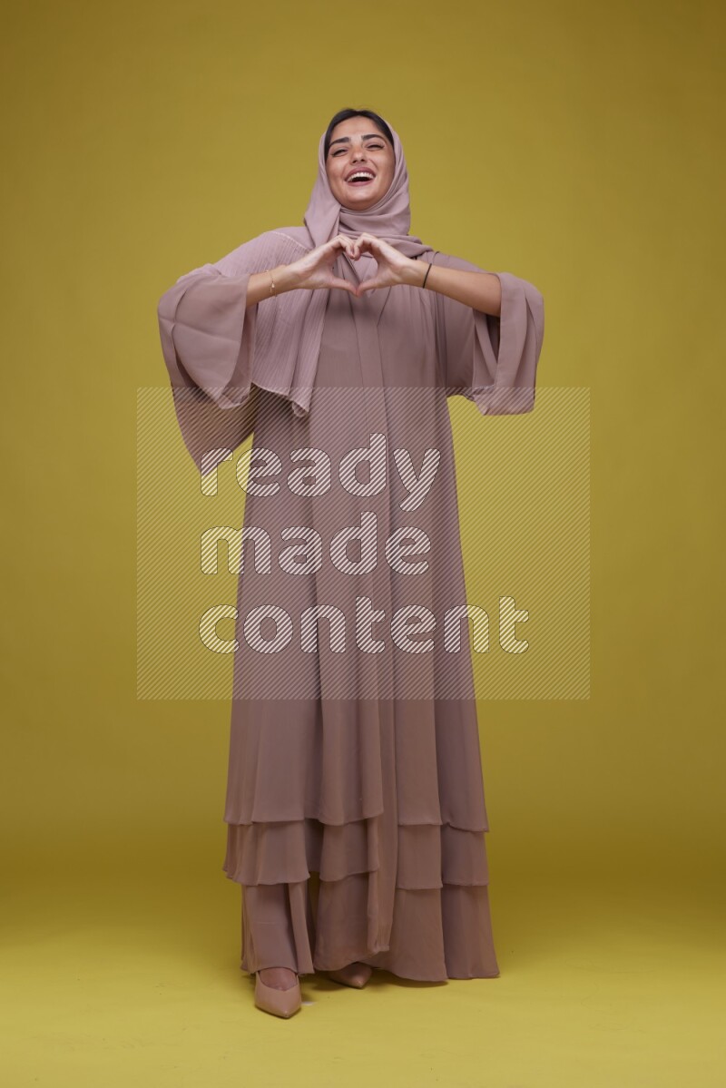 A woman Pointing on a Yellow Background wearing Brown Abaya with Hijab