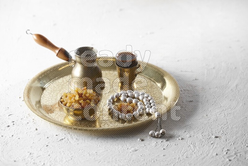 Raisins in a metal bowl with coffee and prayer beads on a tray in a light setup