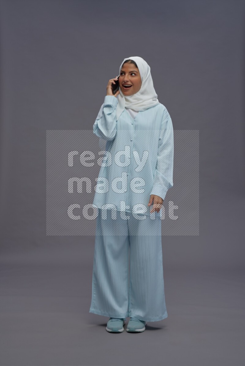 Saudi woman wearing hijab clothes standing talking on phone on gray background