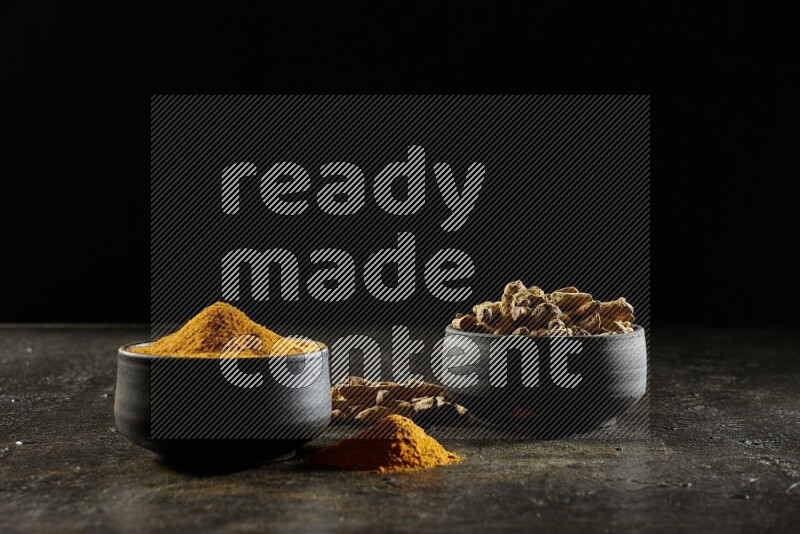 وعاءان من الفخار باللون الأسود، أحدهما ممتلئ ببودرة الكركم والآخر ممتلئ بأصابع كاملة من الكركم المجفف على خلفية سوداء