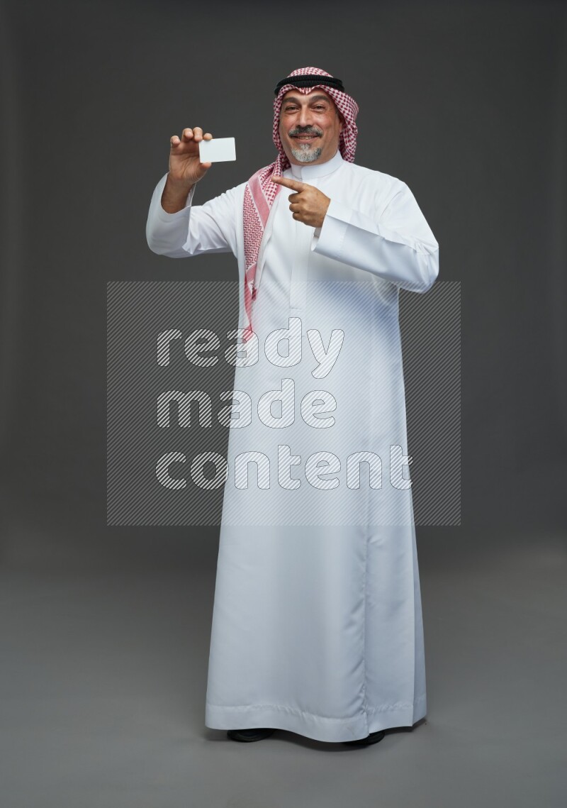 Saudi man with shomag Standing holding ATM card on gray background