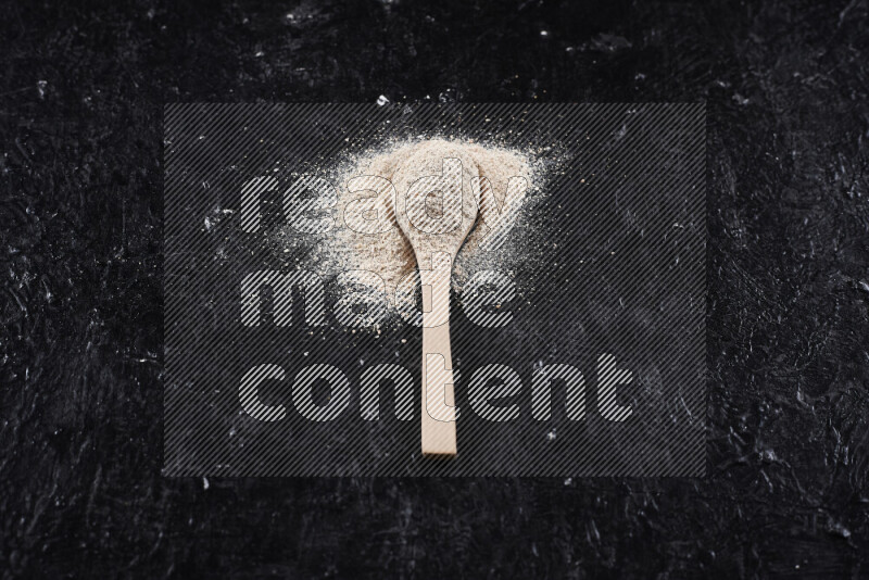 A wooden spoon full of onion powder on black background