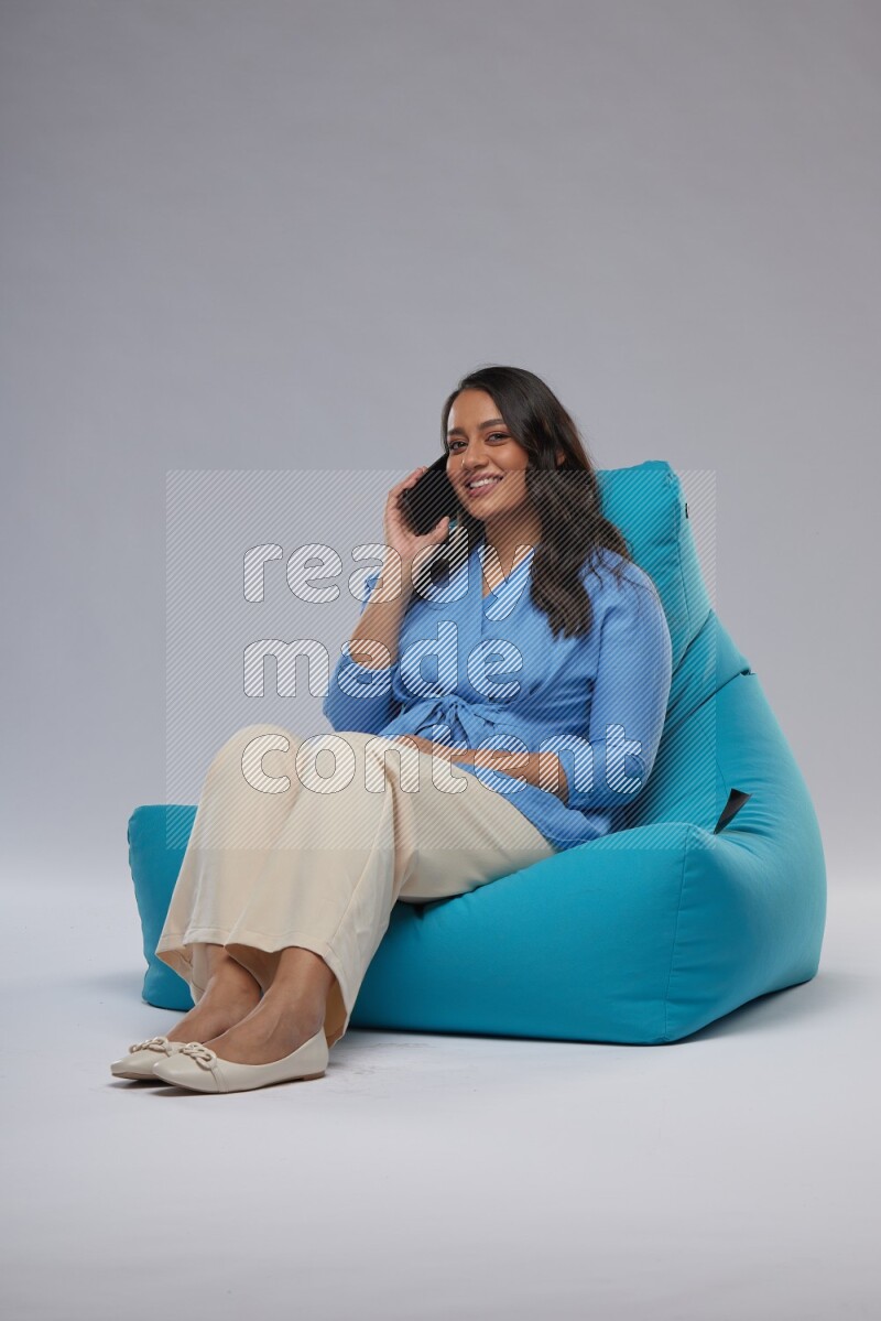 A woman sitting on a blue beanbag and talking on the phone