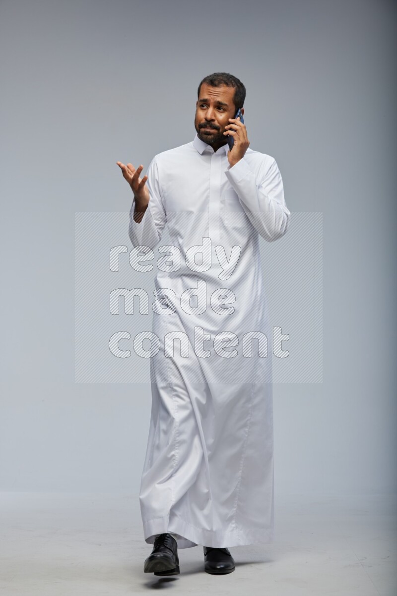 Saudi man wearing Thob standing talking on phone on Gray background