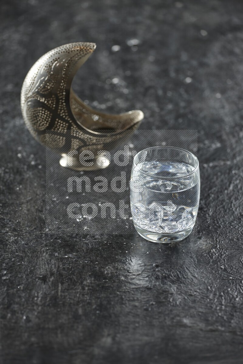A silver lantern with different drinks, dates, nuts, prayer beads and quran on textured black background