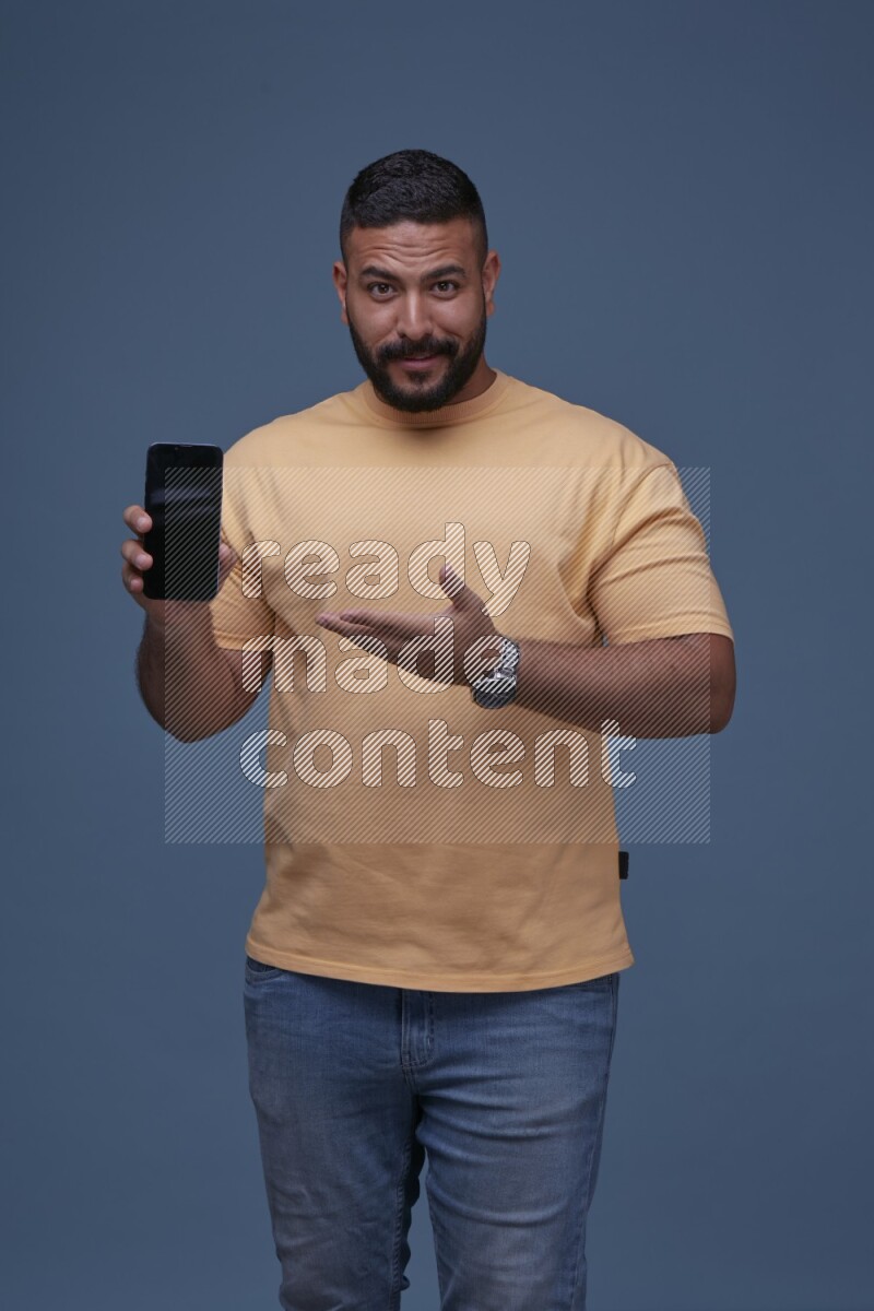 A man Pointing at a Smartphone on Blue Background wearing Orange T-shirt
